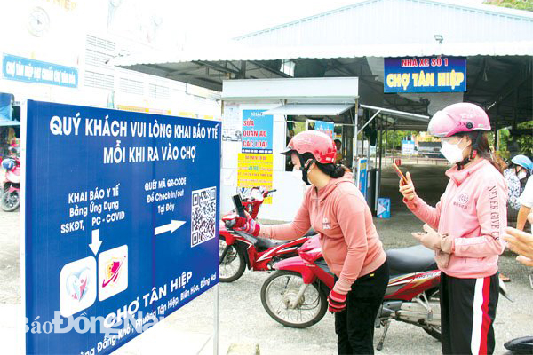 Người dân khai báo y tế bằng mã QR trước khi vào chợ Tân Hiệp (TP.Biên Hòa) mua sắm. Ảnh: H.Quân
