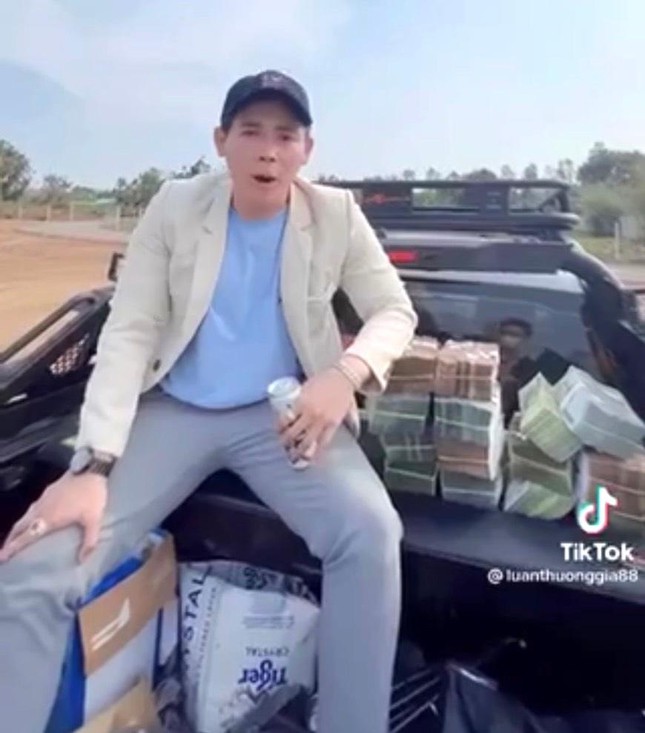 Nam thanh niên mặc vest màu trắng, đầu đội mũ, ngồi sau xe ô tô bán tải, liên tục xếp những cọc tiền có mệnh giá 500 ngàn đồng, 200 ngàn đồng.