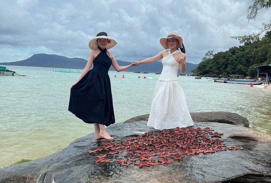 Hai nữ du khách chụp hình bên cạnh xác hàng chục con sao biển bị phơi trên đá nóng. Ảnh: Facebook