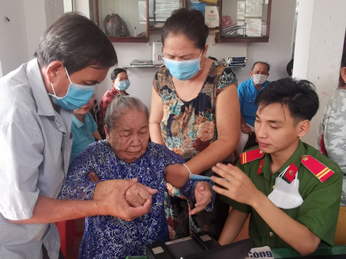 Một cụ già tại phường Long Tuyền khó khăn trong lúc lấy vân tay được công an và người dân giúp đỡ (Ảnh: CACC)