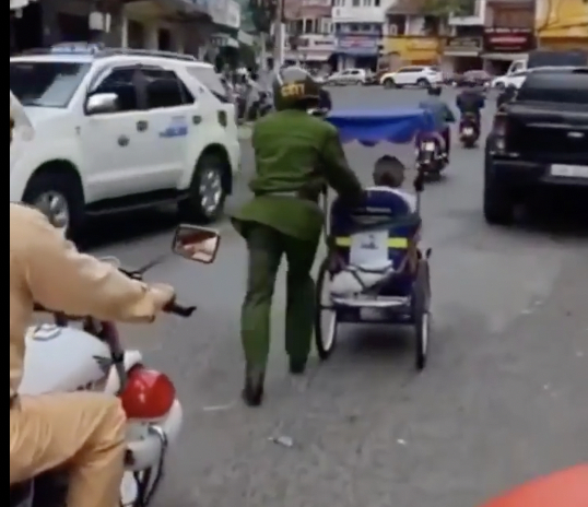 Hình ảnh cảnh sát đẩy xe lăn bị xẹp bánh giúp ông cụ bán vé số khiến nhiều người ấm lòng - Ảnh: cắt từ clip