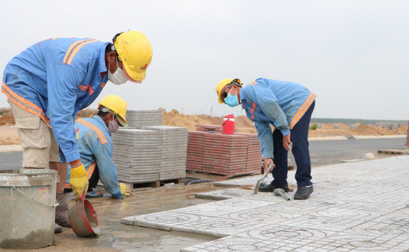 Công nhân đang hoàn thiện việc thi công lát đá vỉa hè một tuyến đường trong khu tái định cư Lộc An - Bình Sơn - Ảnh: H.M.