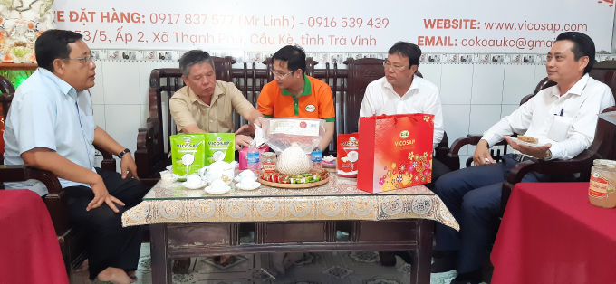Anh Trần Duy Linh (áo cam) giới thiệu quy trình sản xuất kẹo dừa sáp và hủ dừa sáp sợi với ông Ngô Chí Cường - Bí thư Tỉnh uỷ Trà Vinh. Ảnh: MĐ.