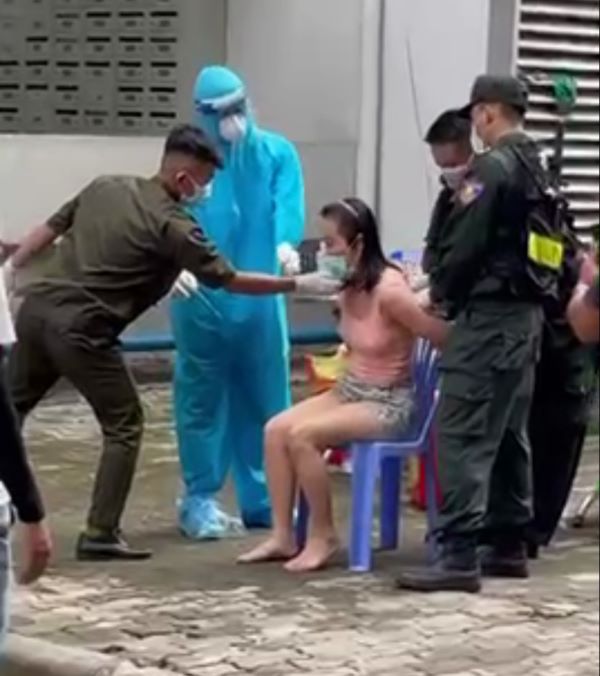 Bà P.L bị giữ hai tay, ngồi trên ghế trước khi nhân viên y tế tiến hành test covid-19.